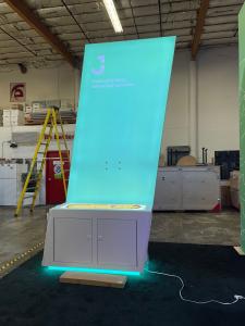 Custom Island Exhibit with Gravitee Tower with Internal Storage, Tension Fabric Graphics, (2) Double-sided Lightboxes with Custom Counters, Locking Storage, (4) Monitor Mounts, and (2) MOD-1458 Charging Tables with Wireless Charging Pads
